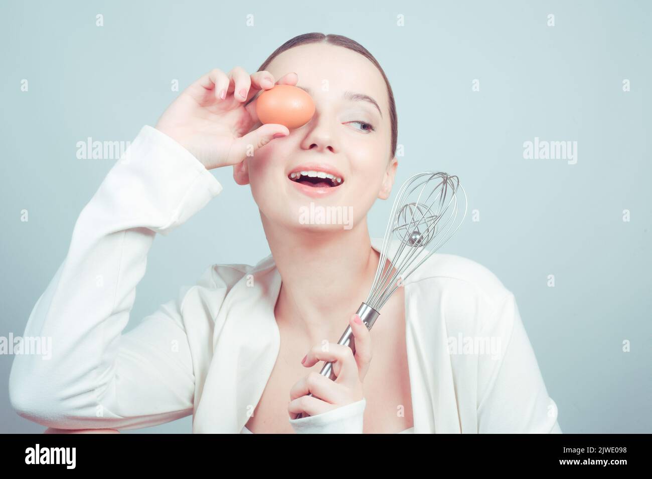 The girl stands in white background, balloon whisk and aggs and cooks