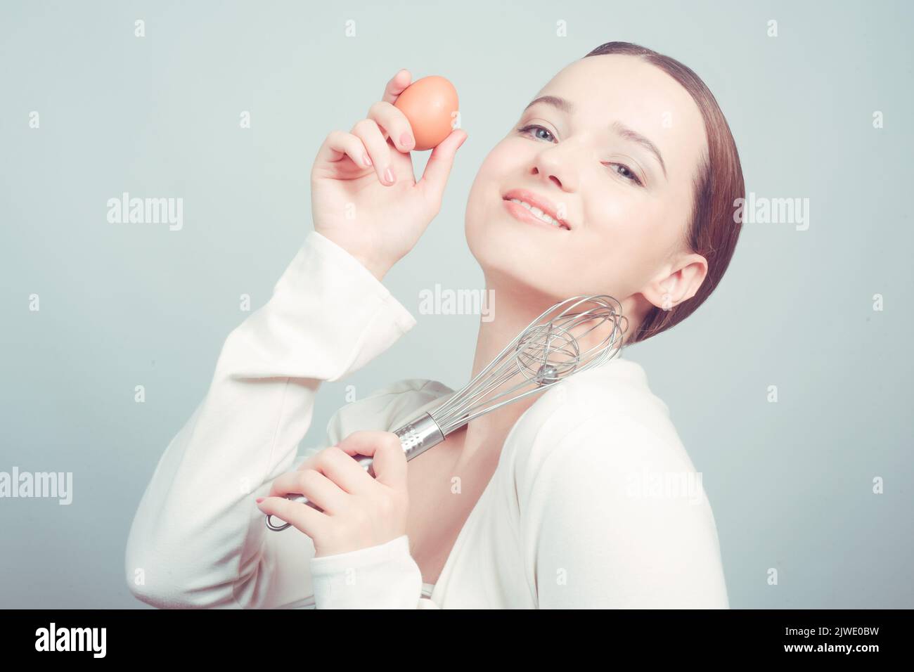 The girl stands in white background, balloon whisk and aggs and cooks