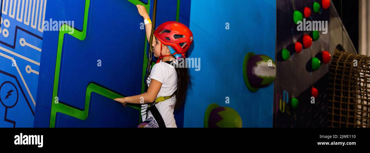 Girl wearing in harness and safety equipment climbing on practical wall