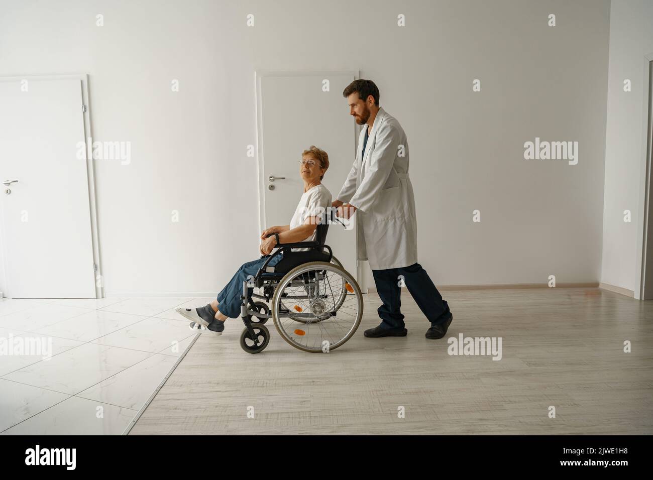 Professional male doctor carrying female patient on wheelchair in