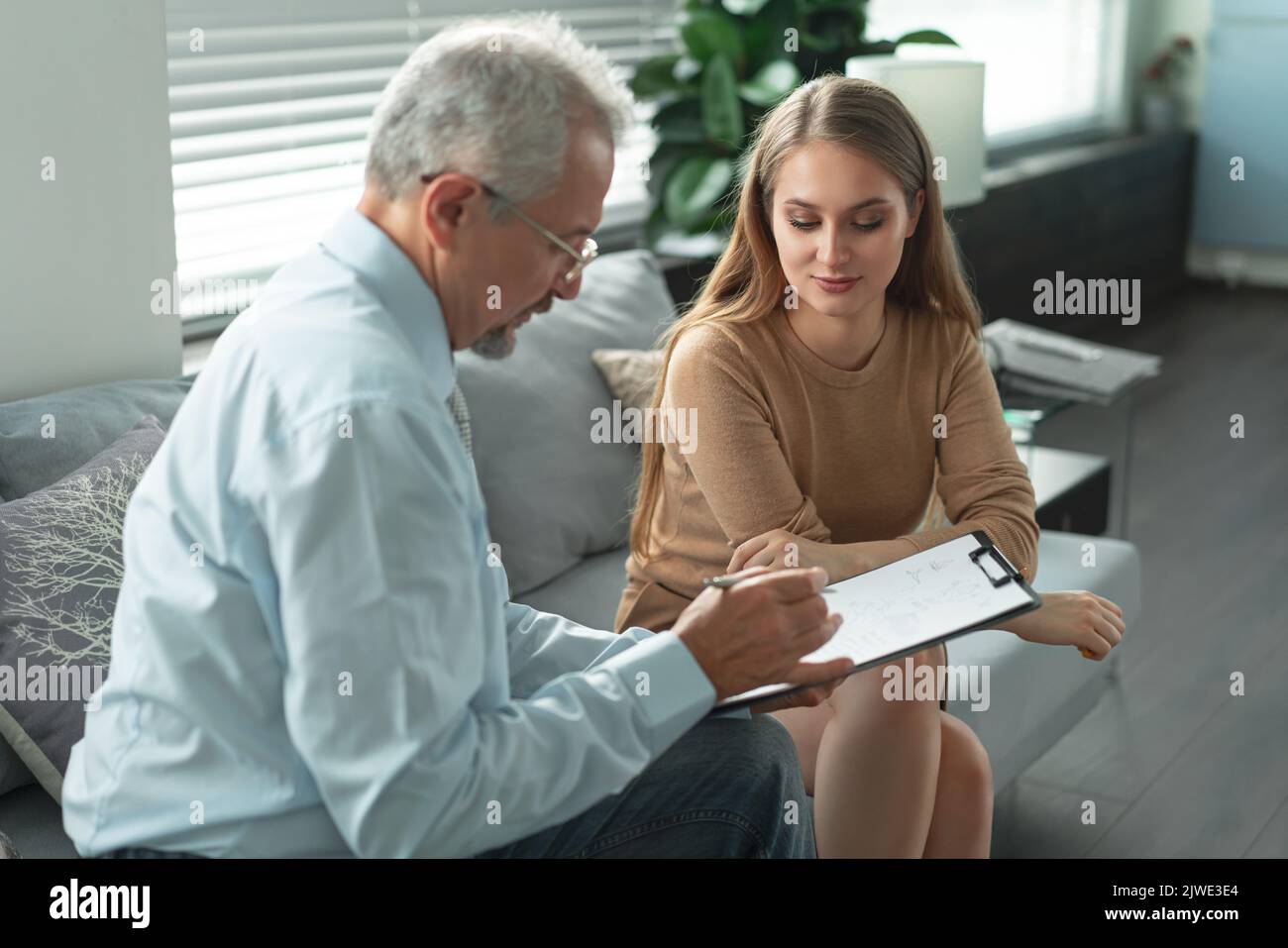 Young woman at a consultation with a psychotherapist. A psychologist has sessions with her patient in the office, giving him advice about his life. Stock Photo
