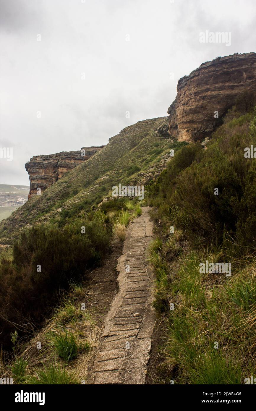 A narrow concrete walking trail going up into the cold and rainy Drakensberg Mountains of the Golden Gate Highlands National Park Stock Photo