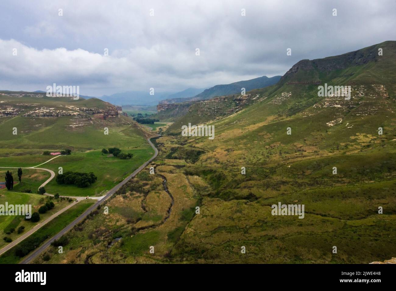 View over the highway cutting through a valley in the Free State Drakensberg Mountains of South Africa, with a storm gathering overhead Stock Photo