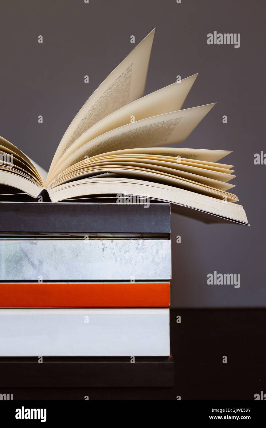 Close-up of an open book on top of pile of books showing half of empty book spine. Concept of reading, literature or knowledge Stock Photo