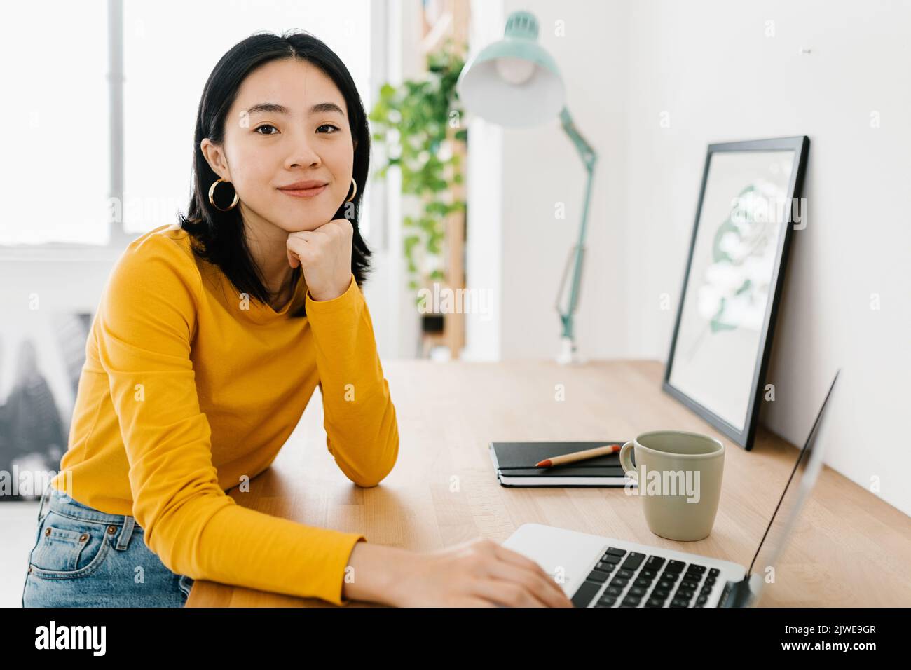 Cheerful young asian woman with laptop smiling at camera sitting at workplace Stock Photo