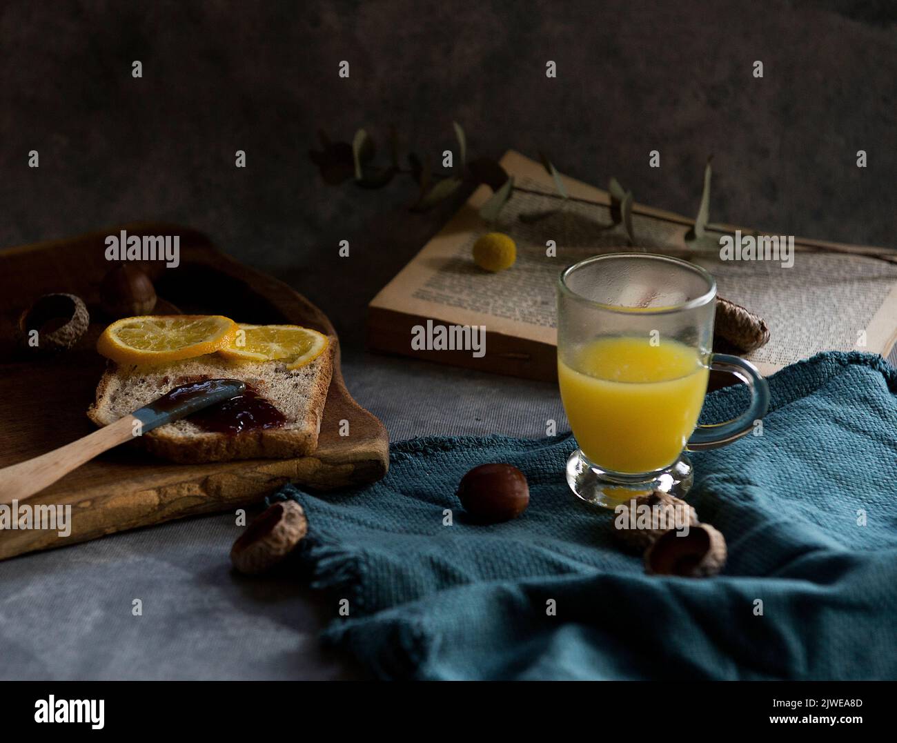 Slice of toast with jam, a glass of orange juice and an open book on a table Stock Photo