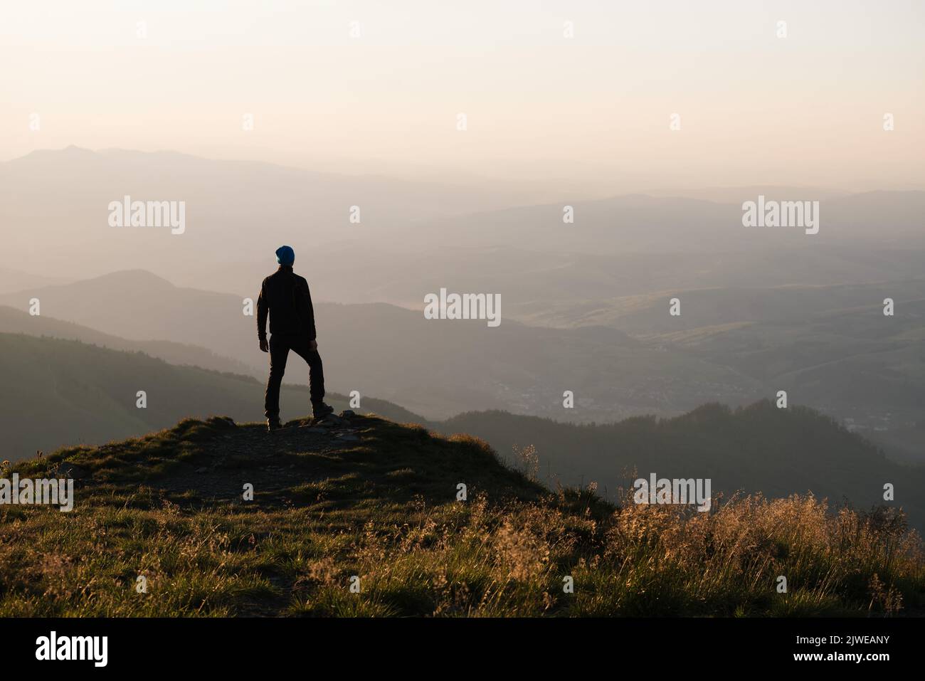 The guy stands on the top of the mountain and enjoys the view of the endless expanses. Healthy lifestyle and mental freedom concept Stock Photo
