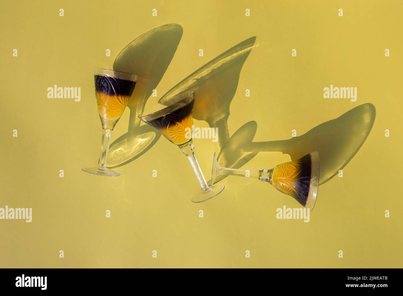 3 crystal glasses with two-color frozen jelly lie on a yellow background, top view. interesting contrasting shadows. Holiday and fun atmosphere. Delic Stock Photo