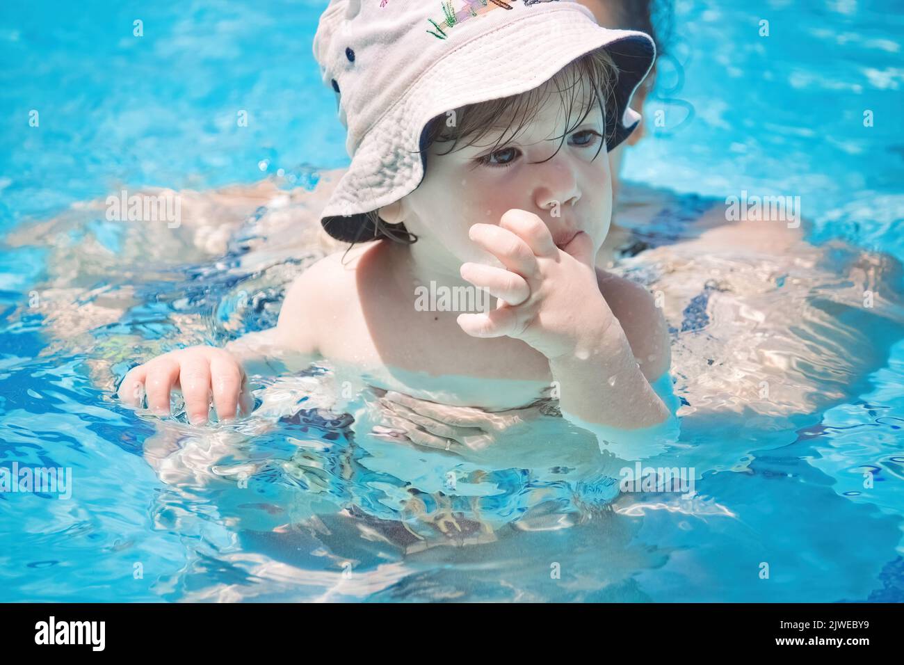 Cute little toddler boy wearing a hat in the swimming pool with his
