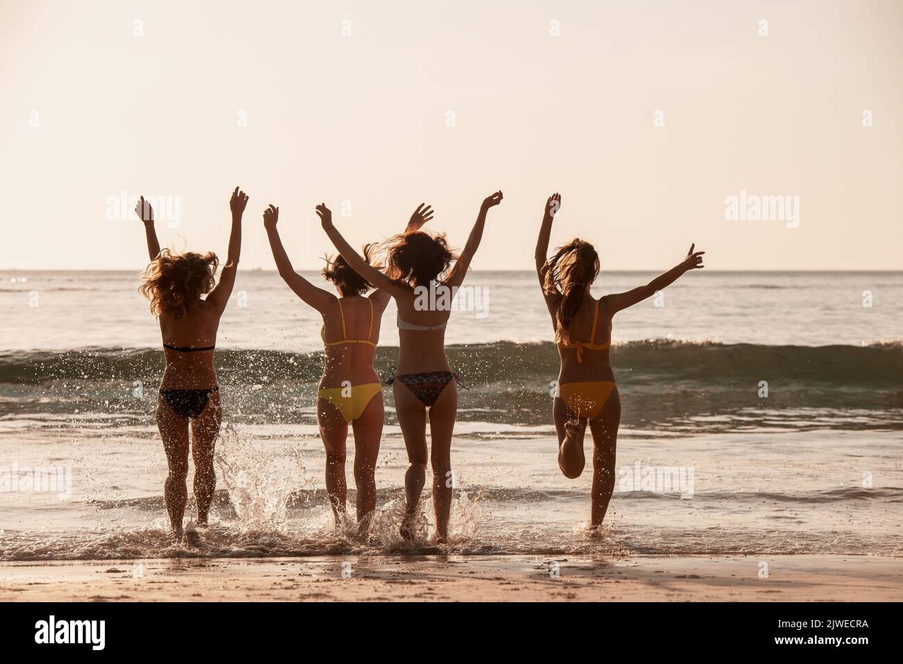 Four happy girls in swimsuits runs and having fun at sunset sea beach. Tropical vacations concept Stock Photo