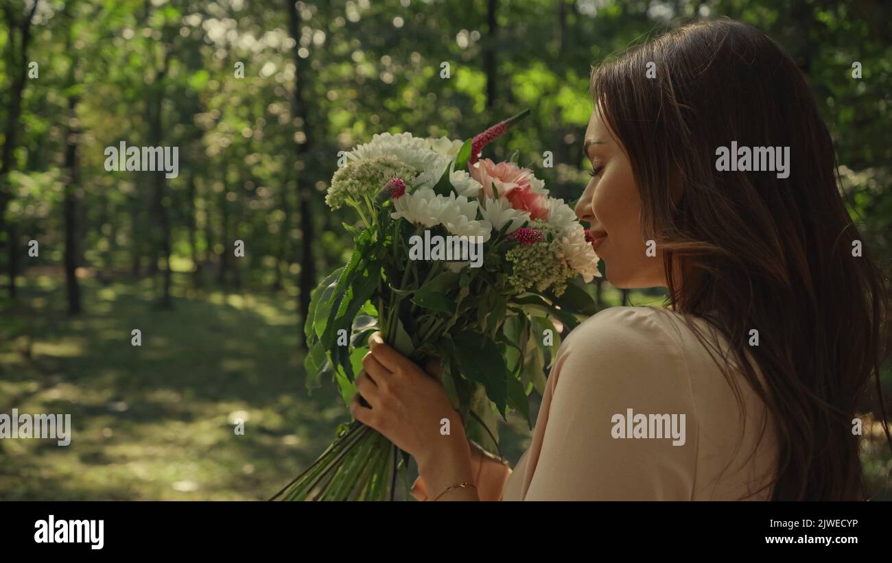 Side view of young woman smelling bouquet of flowers in summer park ...