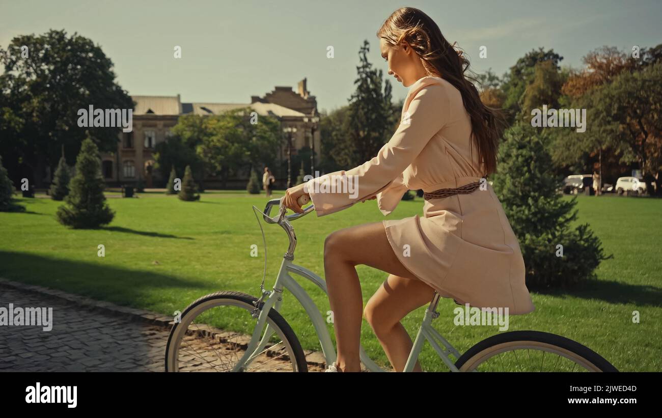 Side view of brunette woman in dress cycling in summer park,stock image Stock Photo
