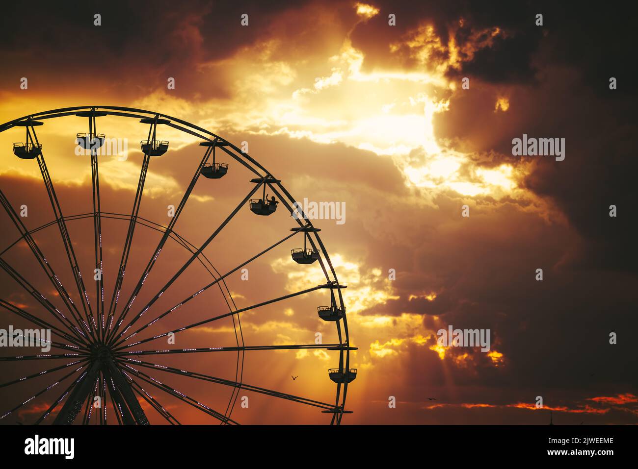 Ferris Wheel and illuminations in amusement park during scenic sunset with dramatic sky clouds and flying birds Stock Photo