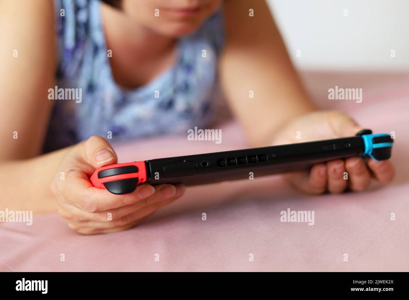 Girl playing game on handheld console lying on a bed, selective focus on a hands Stock Photo