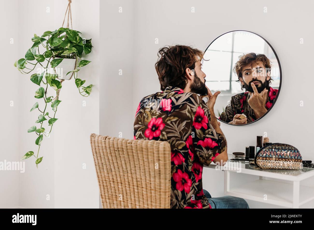 Young adult man putting lip cream in front of the mirror in room at ...