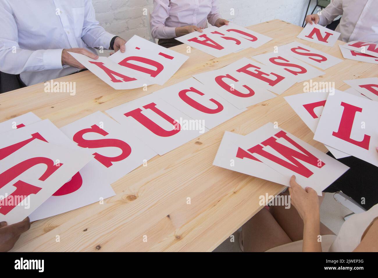 Businesspeople group in business clothes merge letters on paper into word SUCCESS, cooperation unity startup concept Stock Photo