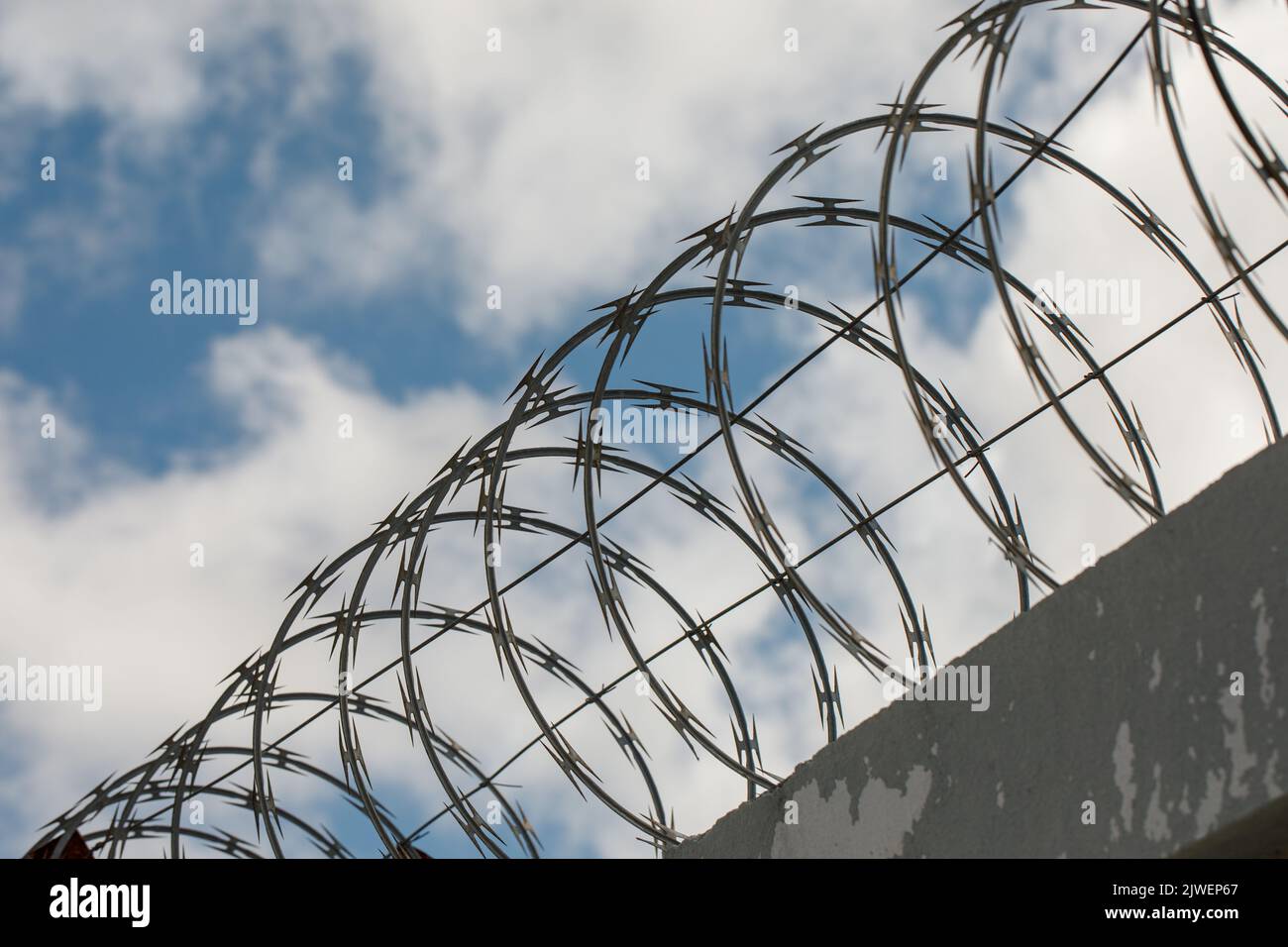 Chain link fence with barbed wire and razor wire. against the blue sky. Stock Photo