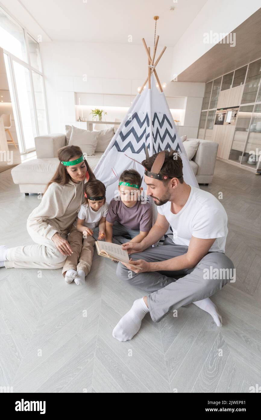 Happy family of parents and two children playing indian at home, wigwam tent, feather roach Stock Photo