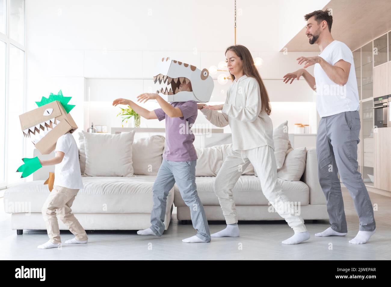 Happy family of parents and two children playing dinosaurs at home, children wearing handmade costume mask of cardboard Stock Photo