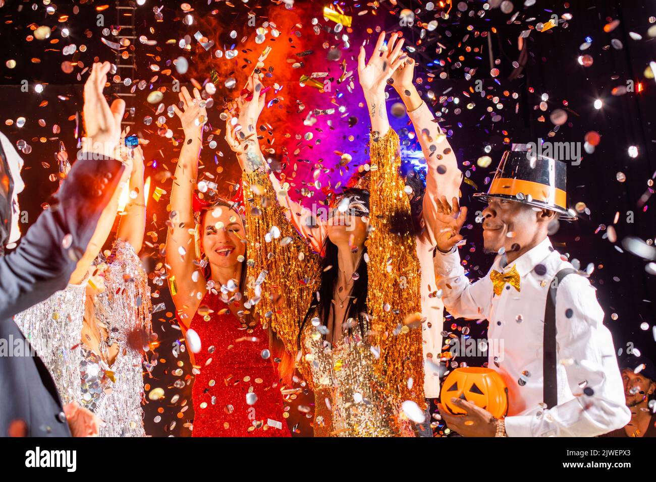 People dance at Halloween party with champagne glasses. Friends in the costumes in nightclub Stock Photo