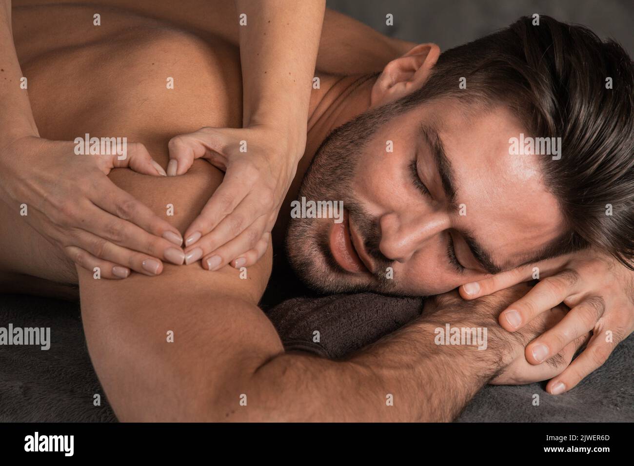 A good-looking man getting a back massage lying down at spa, Woman hand making sign heart love concept Stock Photo