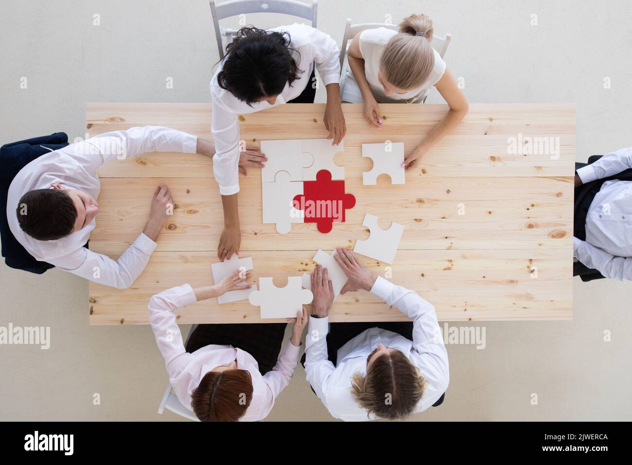 Diverse business people helping in assembling puzzle, cooperation in decision making, team support in solving problems and corporate group teamwork co Stock Photo