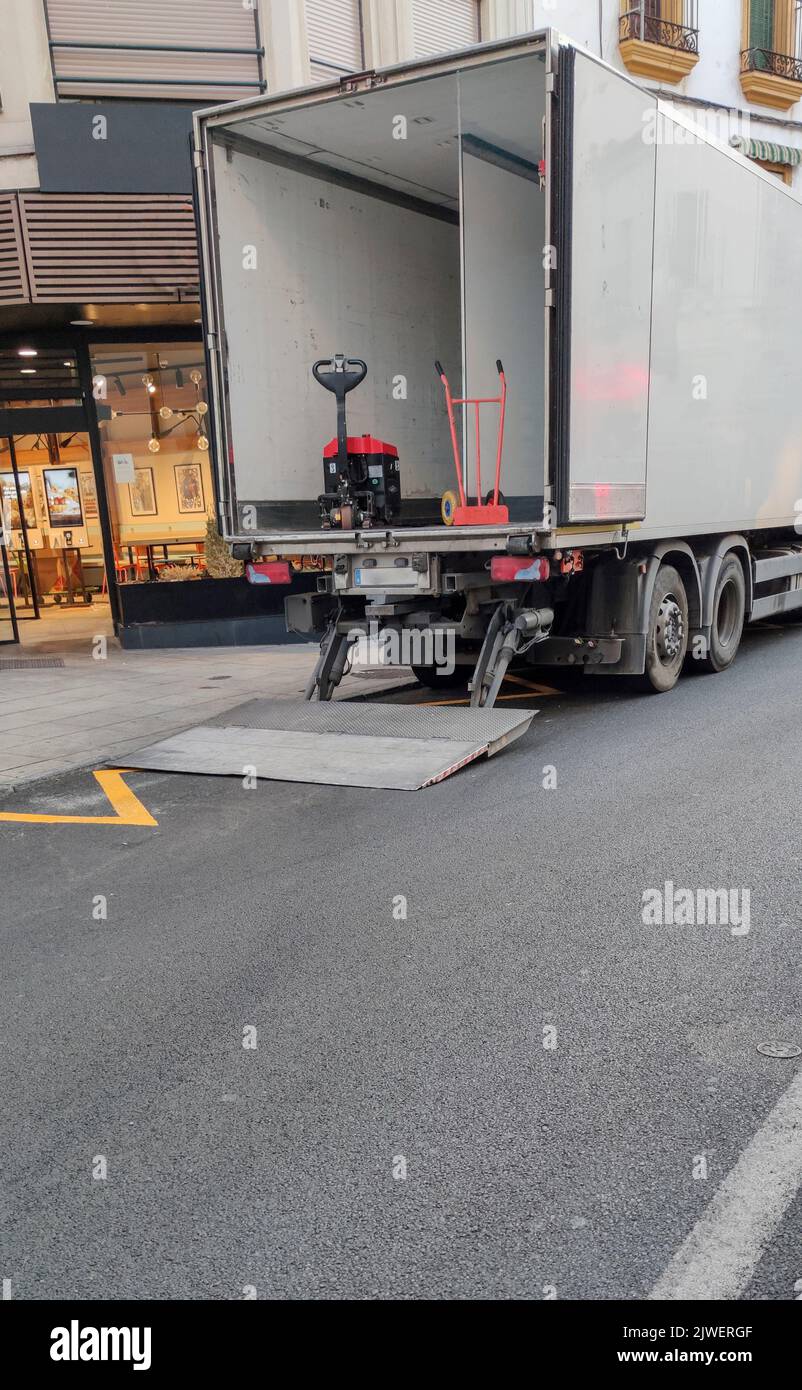 Semi-trailer truck unloading goods at downtown. The truck is equipped with lift ramp Stock Photo