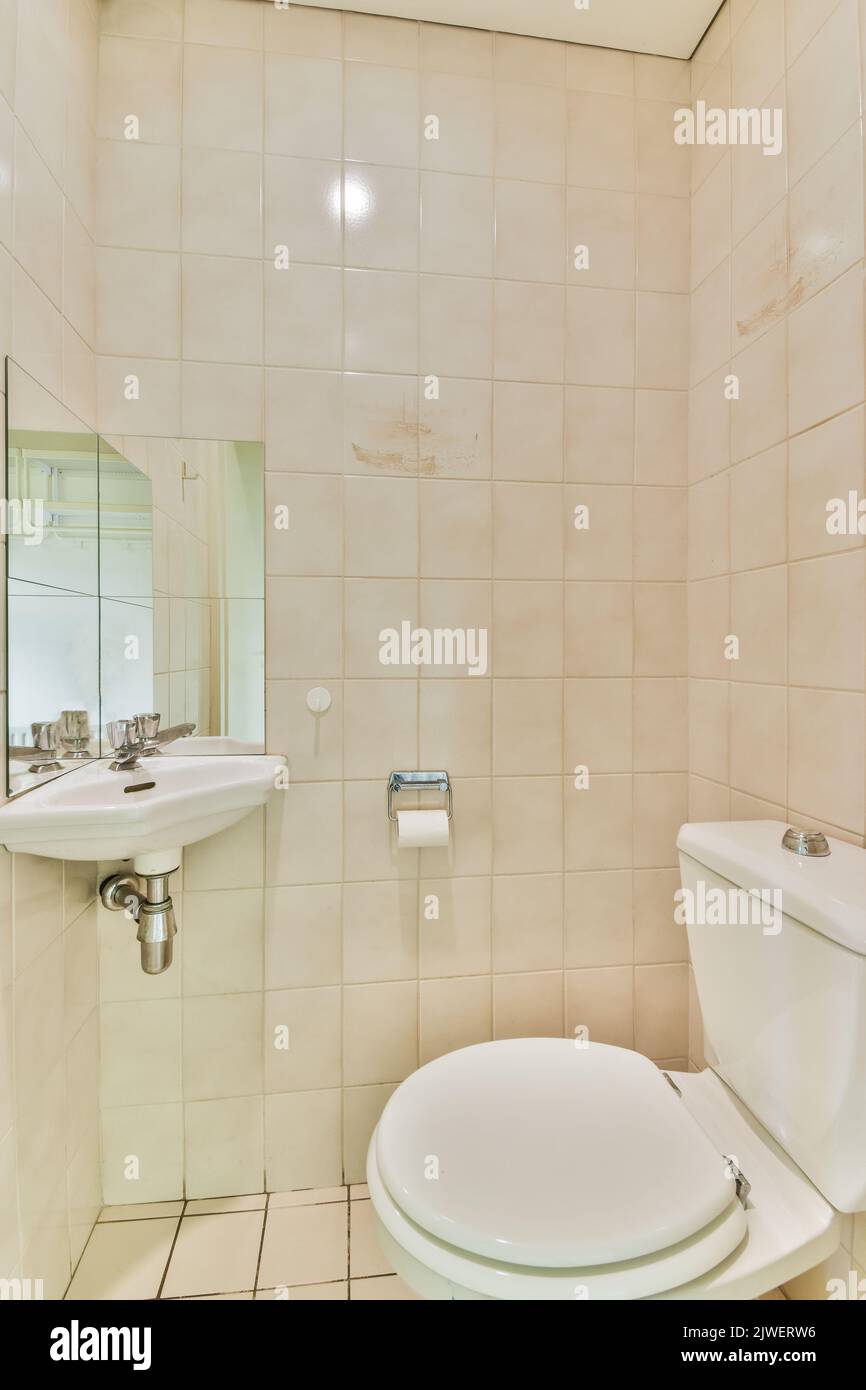 Wall hung toilet and small sink in corner in lavatory room with beige