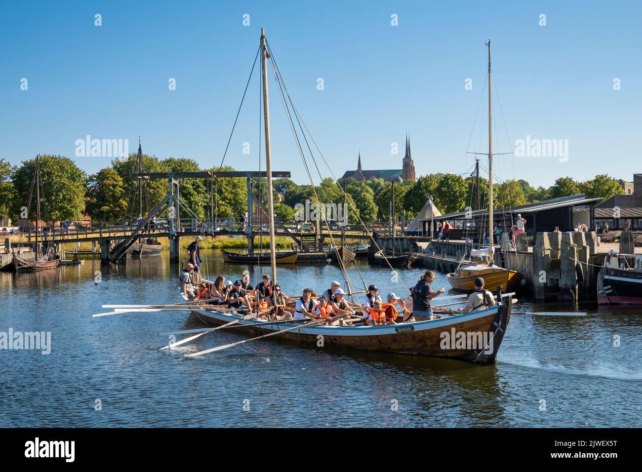 Replica viking ship rowing back in to the Viking Ship Museum with gothic cathedral behind, Roskilde, Zealand, Denmark, Europe Stock Photo