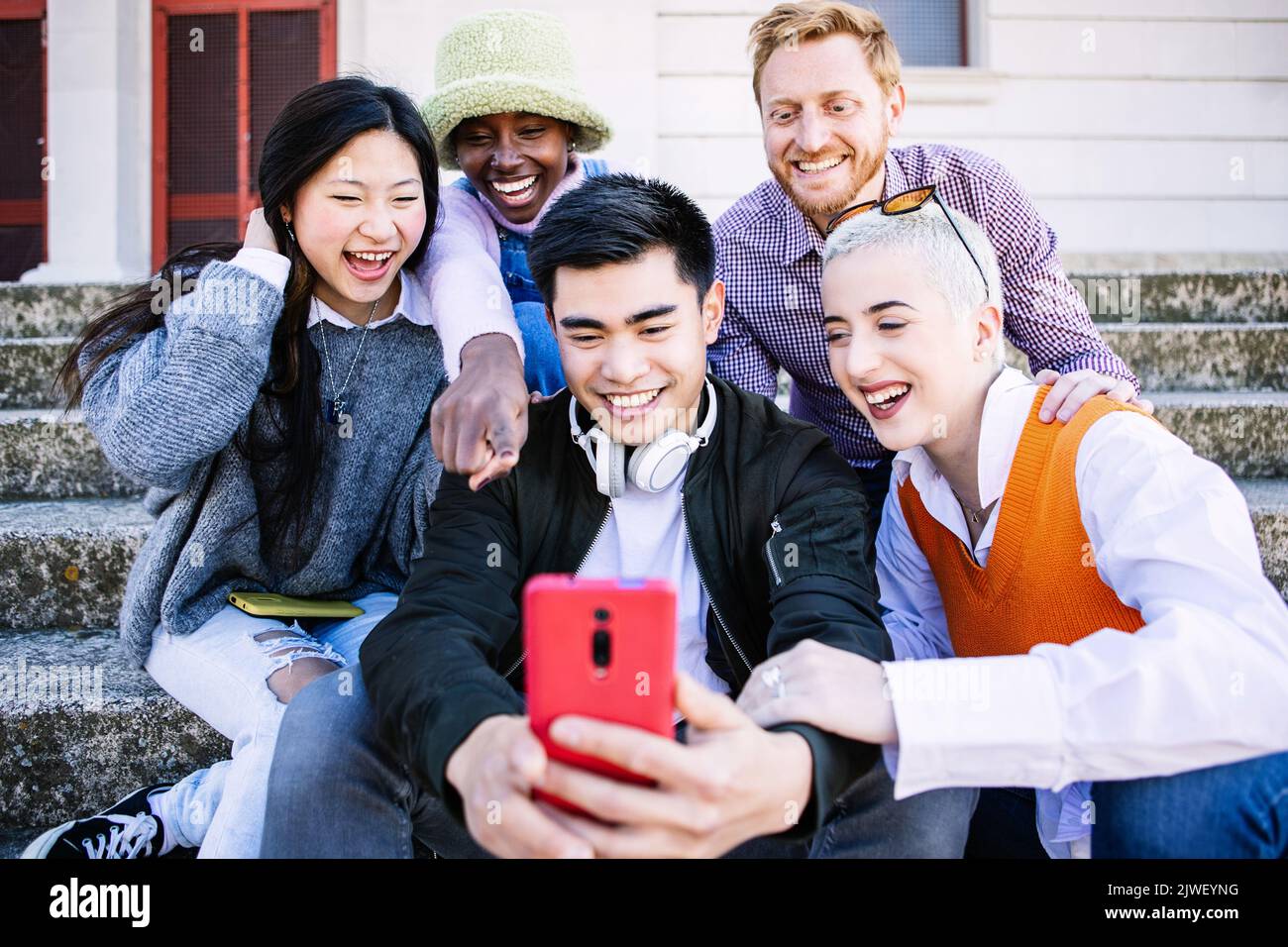 Happy group of young people having fun using mobile phone together outdoors Stock Photo