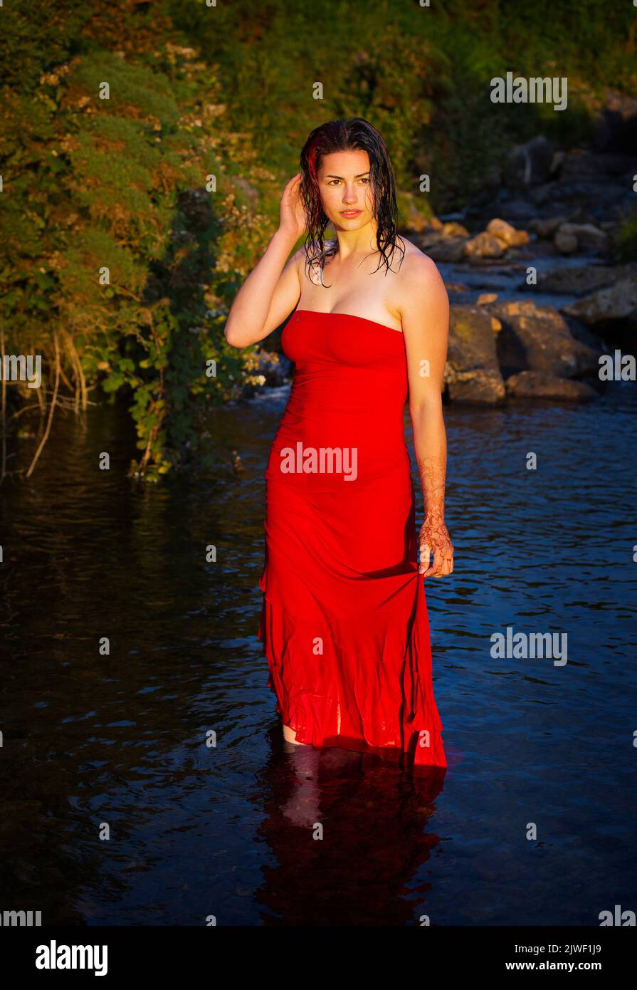 A beautiful young woman with a red dress cooling off in a river Stock Photo
