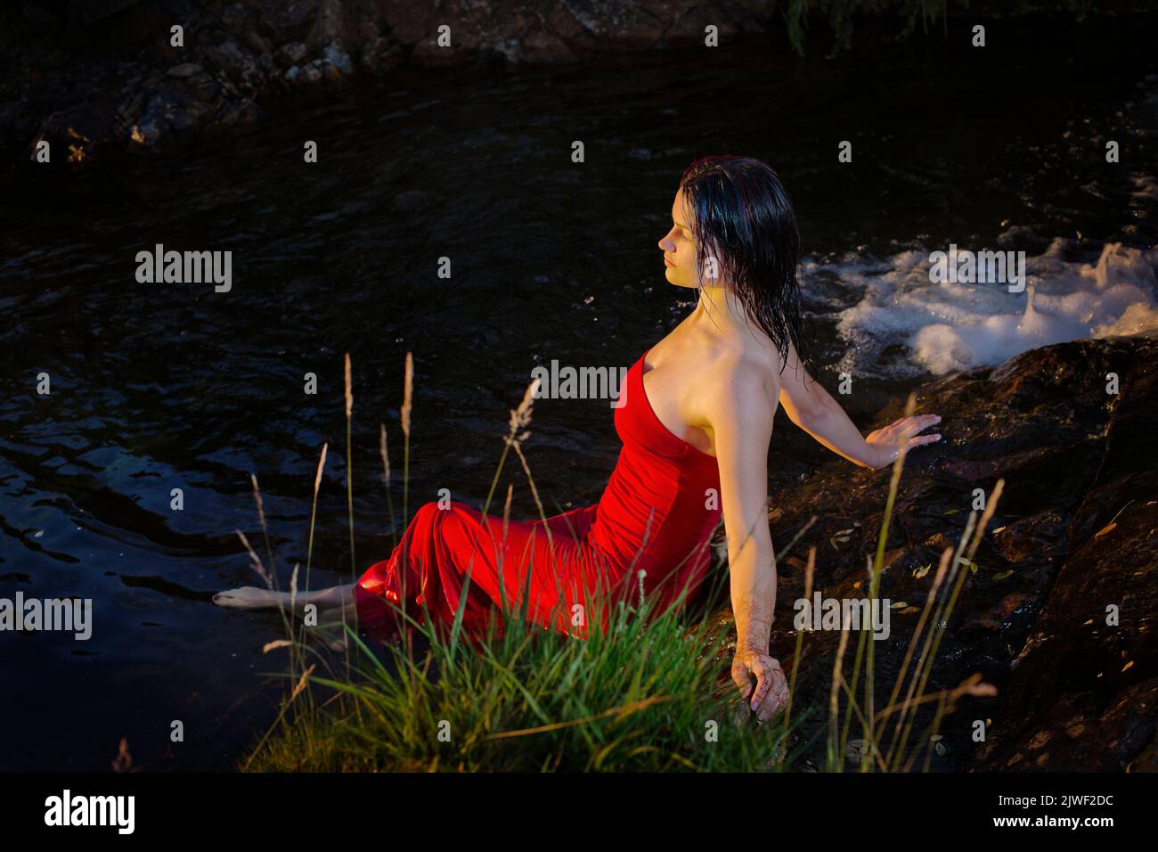 A beautiful young woman with a red dress cooling off in a river Stock Photo