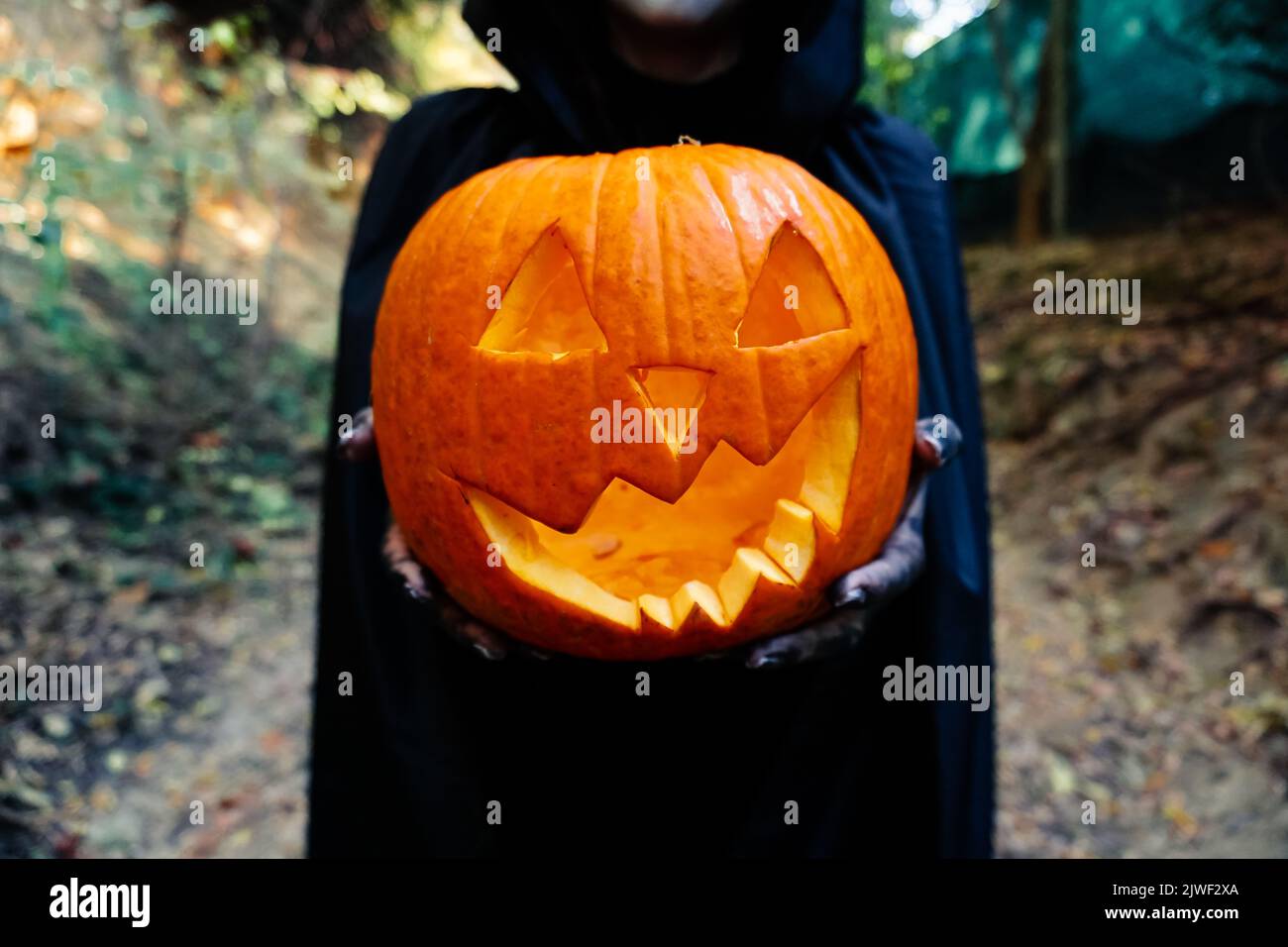 Young woman with halloween paint face mask wearing black hood Scary