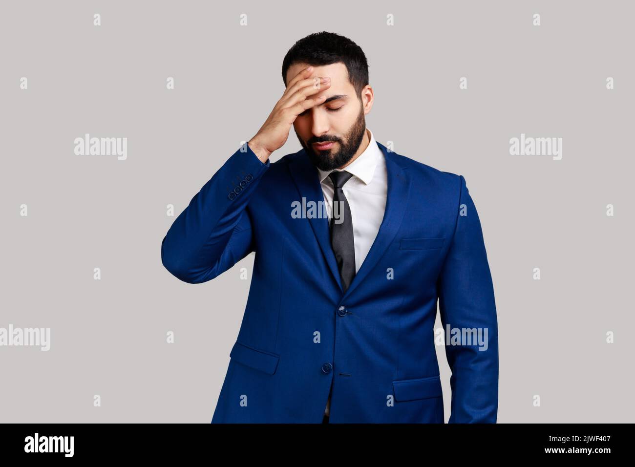 Depressed bearded man making facepalm gesture, feeling regret and shame about forgotten event, bad memory, wearing official style suit. Indoor studio shot isolated on gray background. Stock Photo
