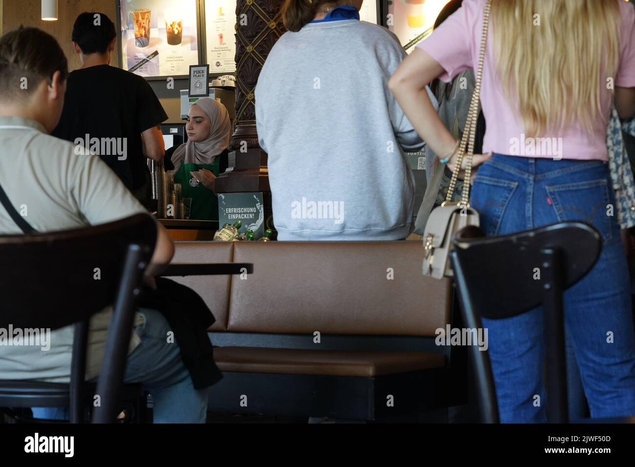 Cutomers standing around the counter in a Starbucks café in Hamburg, Germany. Persons waiting for the coffee are captured in rear view.l Stock Photo
