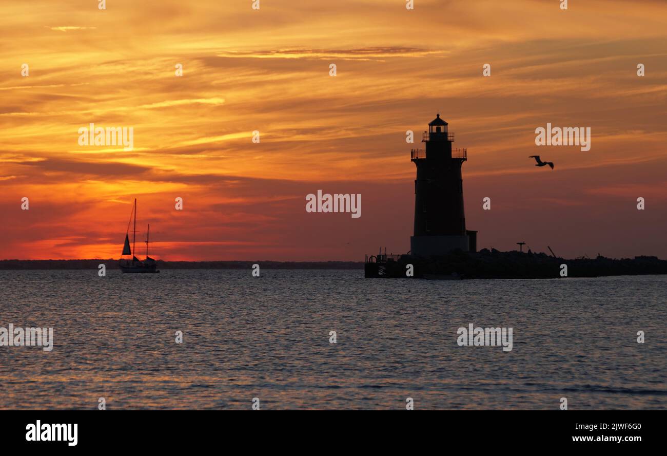 Silhouette of the lighthouse and a yacht during sunset near Cape Henlopen State Park, Lewes, Delaware, U.S.A Stock Photo