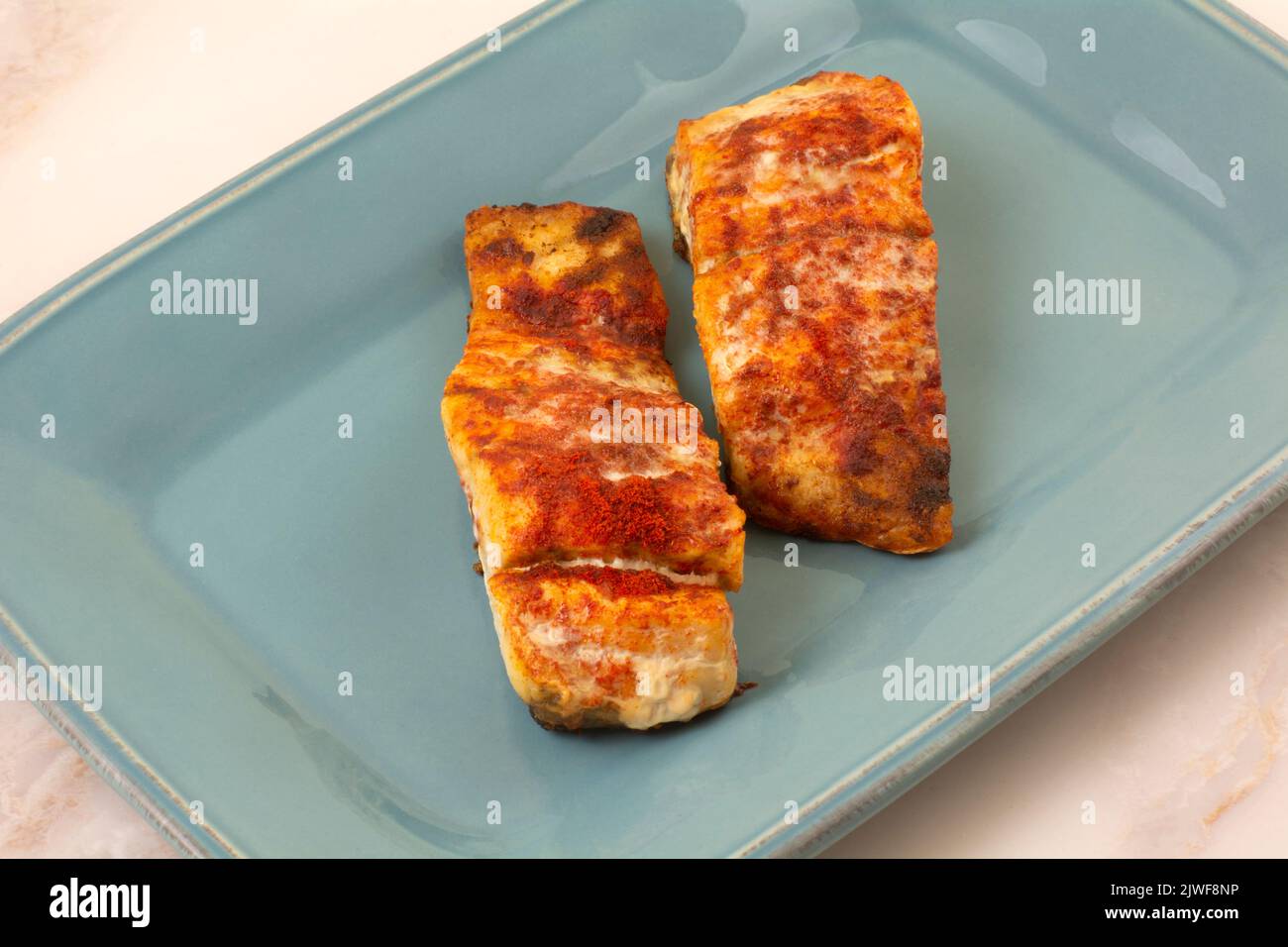 Two baked barramundi fish fillet slices with paprika spice rub on blue