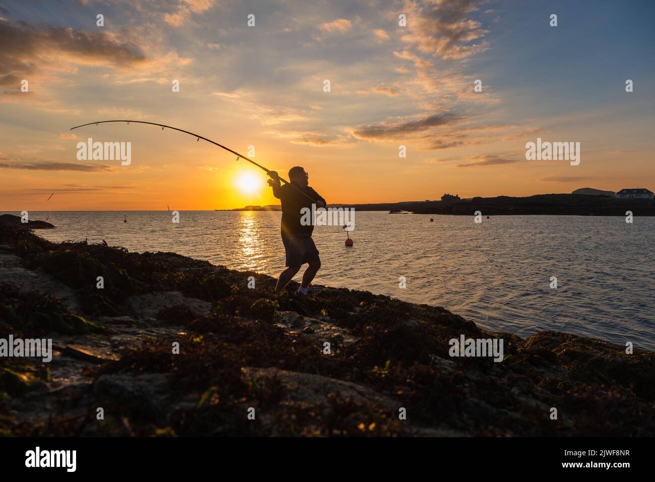 Man casting a fishing line into the sea at Trearddur Bay, Anglesey, Wales Stock Photo