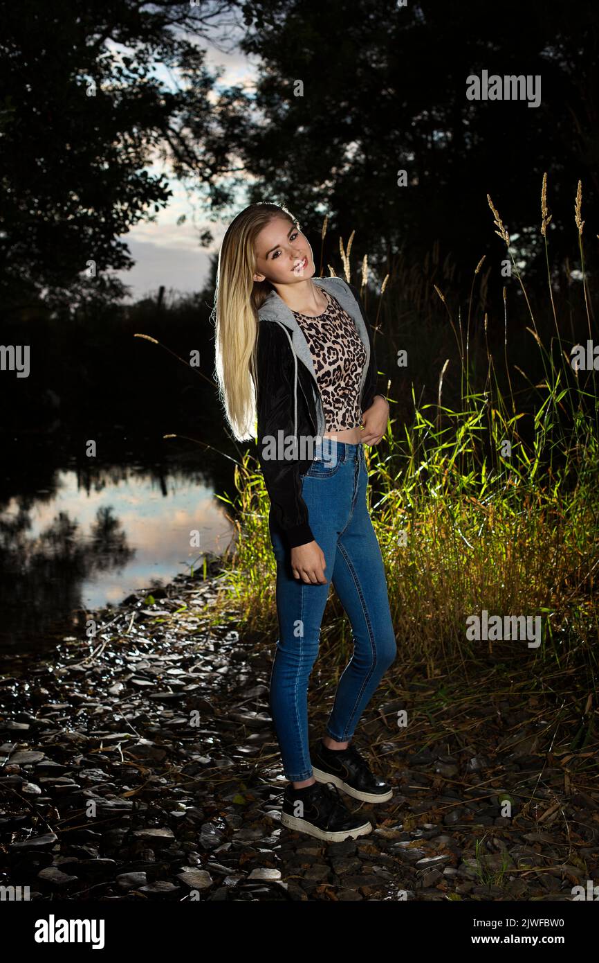 A blonde teenager wearing jeans outdoors by a riverbank Stock Photo