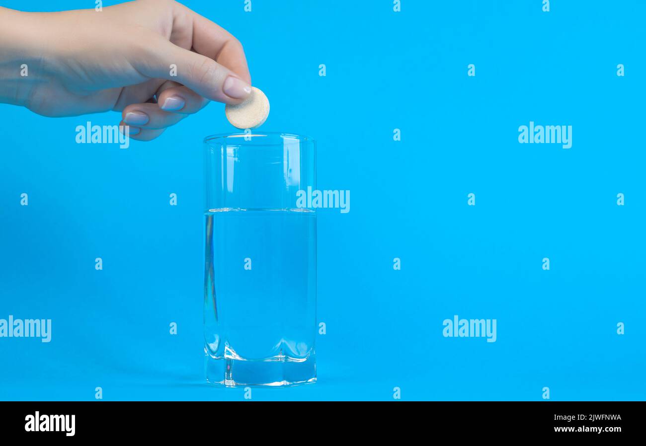 Recovery concept. A woman's hand throws an effervescent pill into a glass of water on a blue background. Place for text Stock Photo