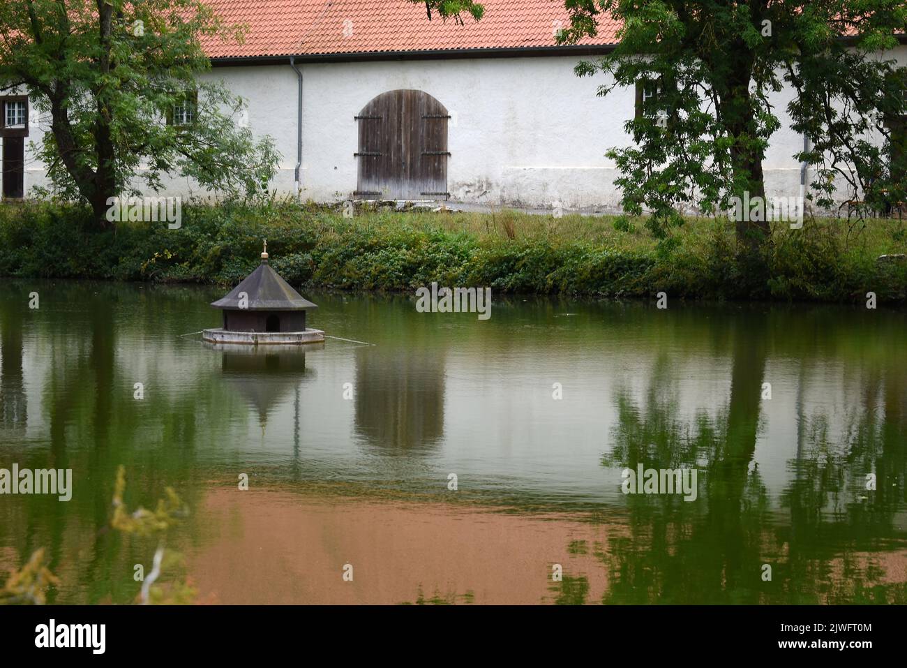 duck house on a lake with reflection of building and trees in the green water Stock Photo