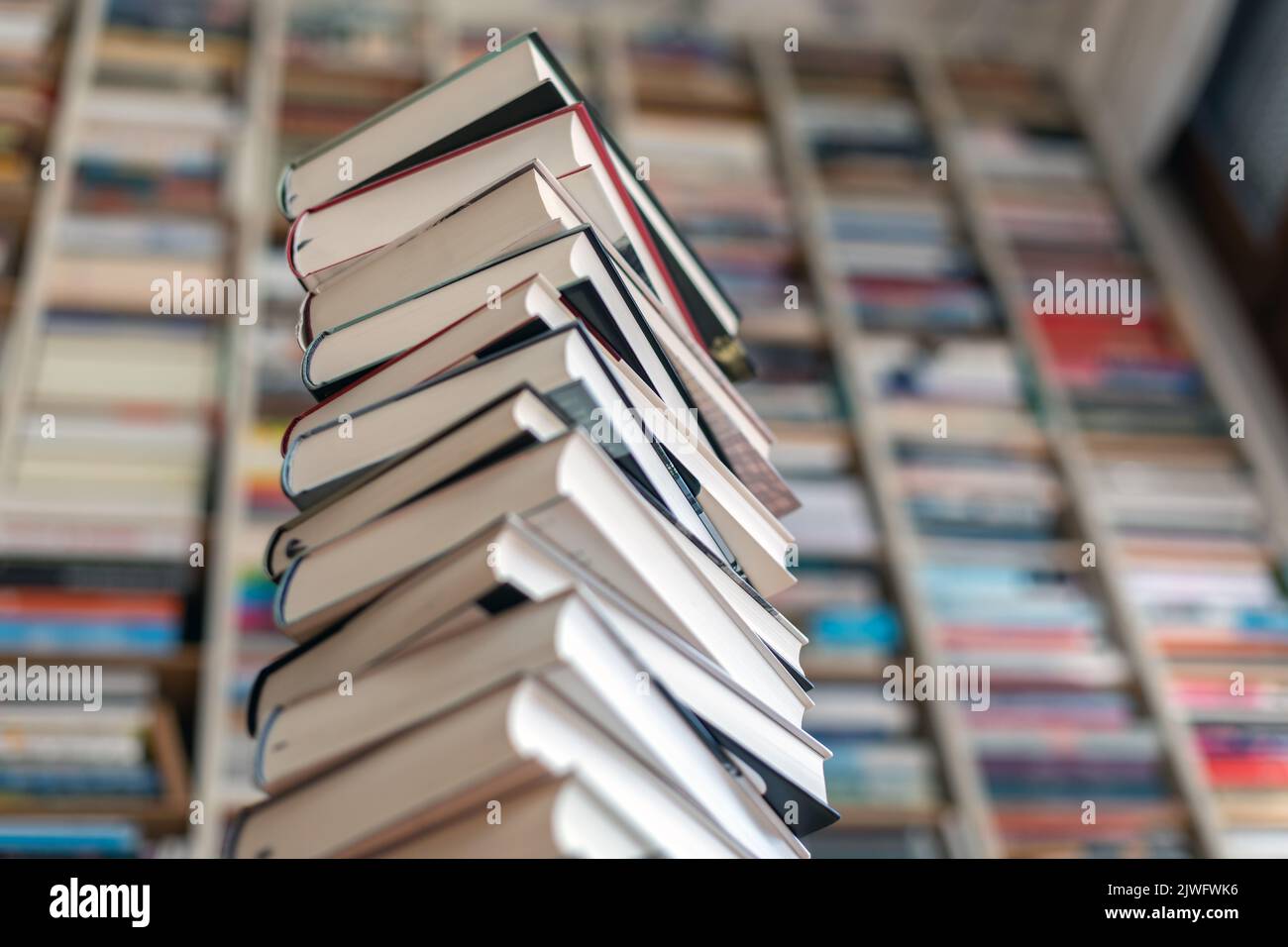 tower of stacked novels in front of book wall Stock Photo