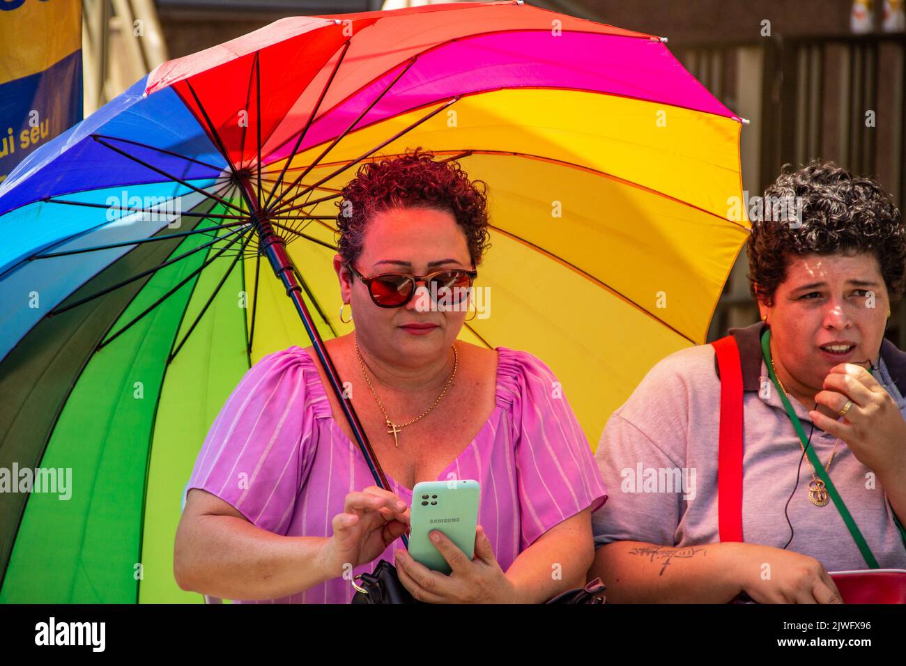 Goiânia, Goias, Brazil – September 05, 2022:A woman holding an umbrella and using a cell phone next to another woman talking into the cell. Stock Photo