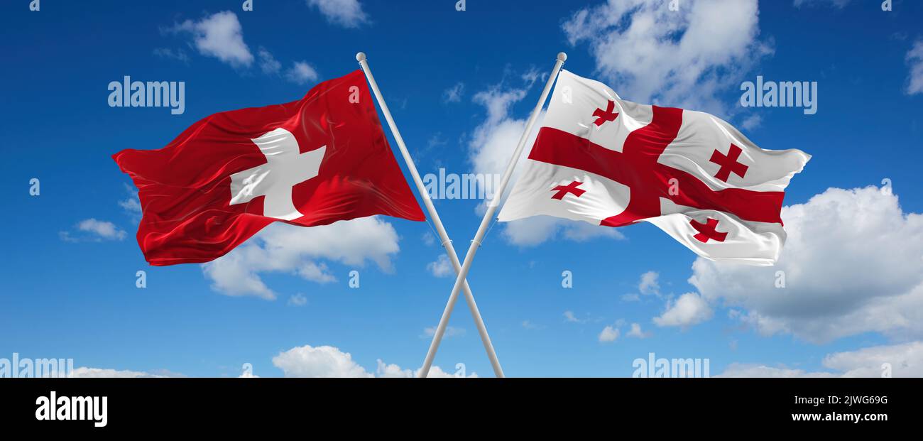 two crossed flags Georgia and Switzerland waving in wind at cloudy sky ...