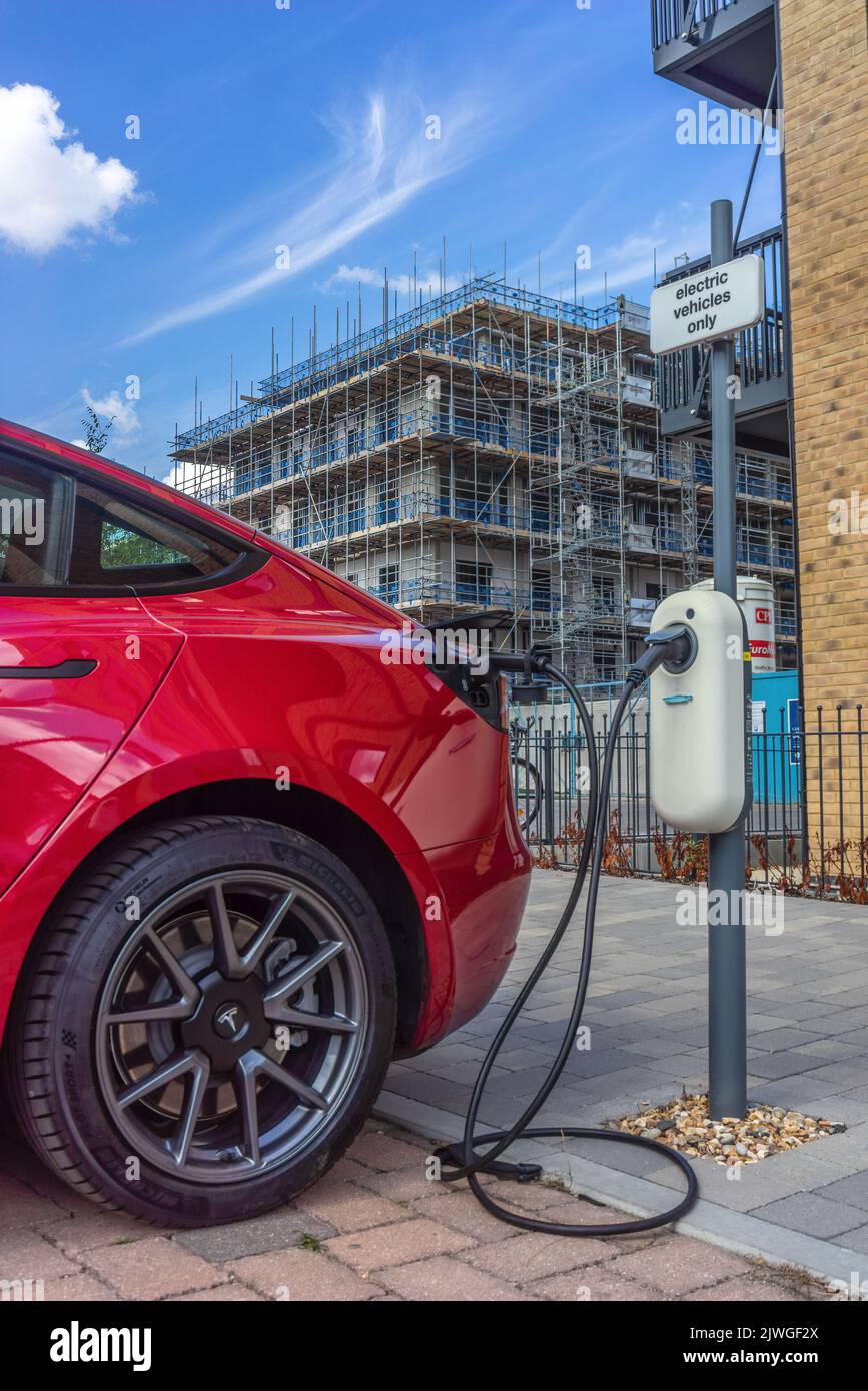 A red Tesla car is charging its car battery at an electrical vehicle