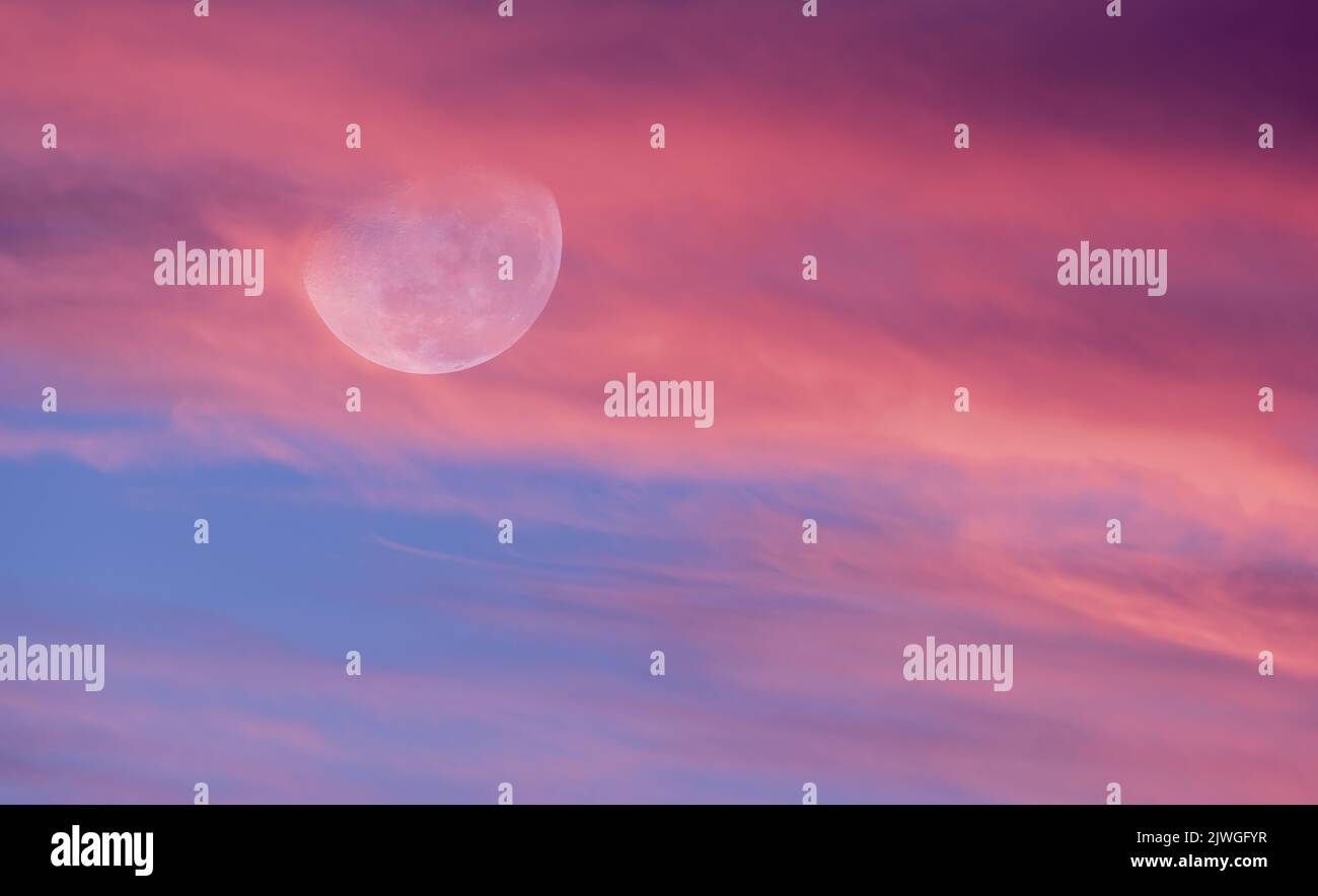 The Moon Is Rising Among A Colorful Cloud Filled Sunset Sky Stock Photo