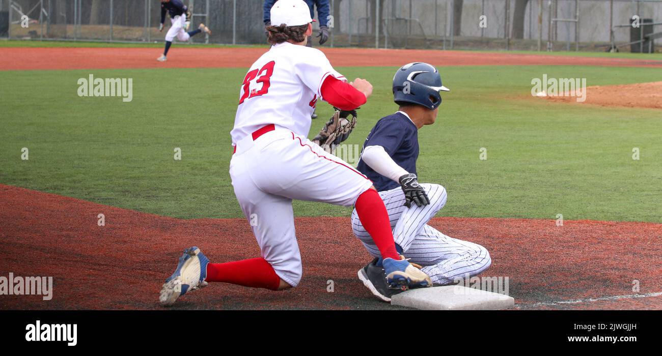 A high school baseball player sliding into third base with third baseman applying the tag during