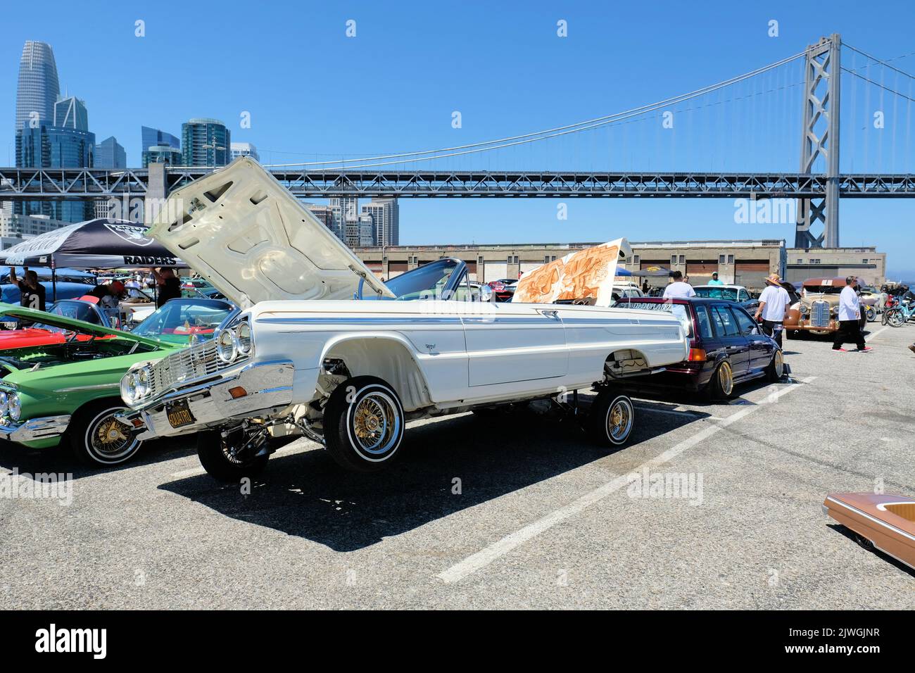 A white 1964 Chevy Impala lowrider car with raised hood and hydraulic system engaged with the Bay Bridge in the background; San Francisco, California. Stock Photo