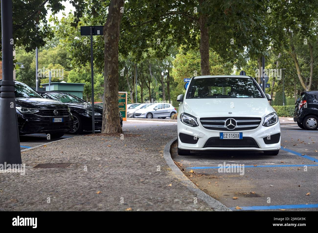 White  Mercedes Benz C180 in a public parking next to a park on a cloudy day Stock Photo