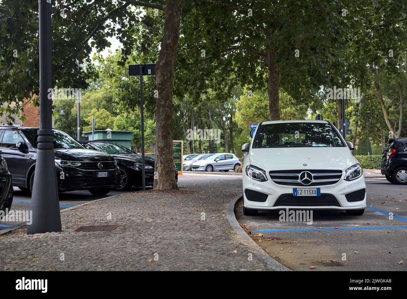 White  Mercedes Benz C180 in a public parking next to a park on a cloudy day Stock Photo